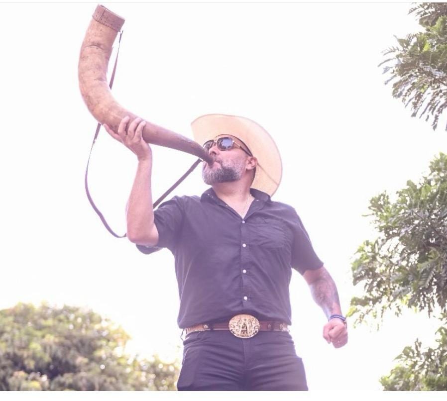 Jeff da RAM tocando berrante, fotografado de baixo contra o céu